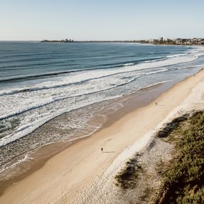 The beaches of Maroochydore seen from above, with gentle waves rolling onto the wide golden sand on a clear, sunny day.